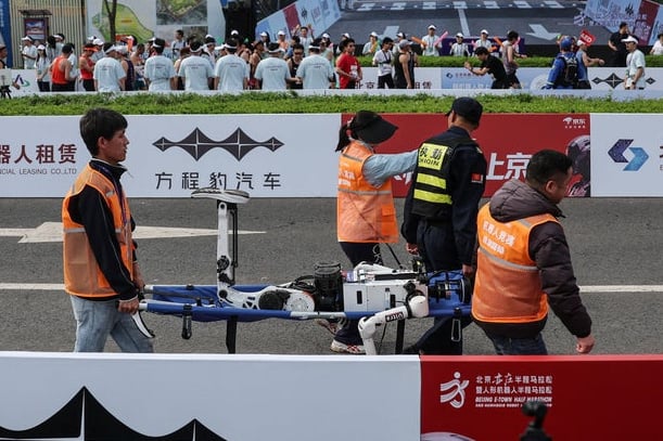 Pracovníci odnáší humanoidního robota, který havaroval po proběhnutí cílové čáry.