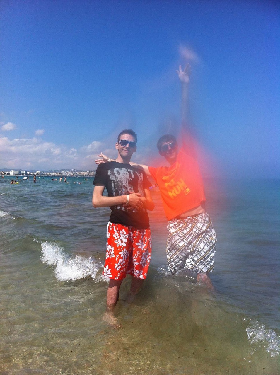 Dva muži ve vodě na pláži, tričko LOST, zvednutá ruka