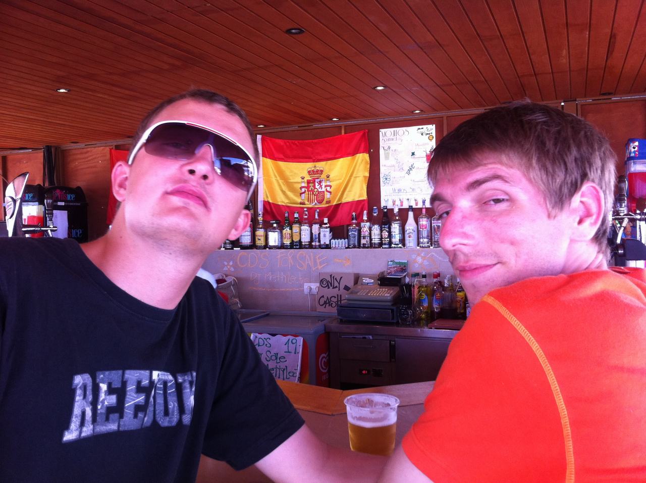 Dva muži u baru, pivo, lahve, španělská vlajka, nápisy RETRO a ONLY CASH.