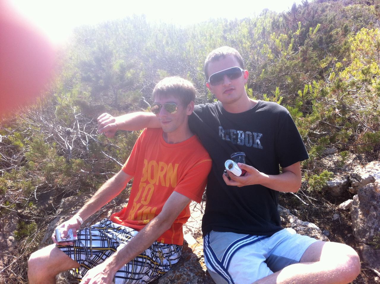 Dva muži v brýlích sedí na kamenech, drží plechovku; trička BORN TO RUN, REEBOK.