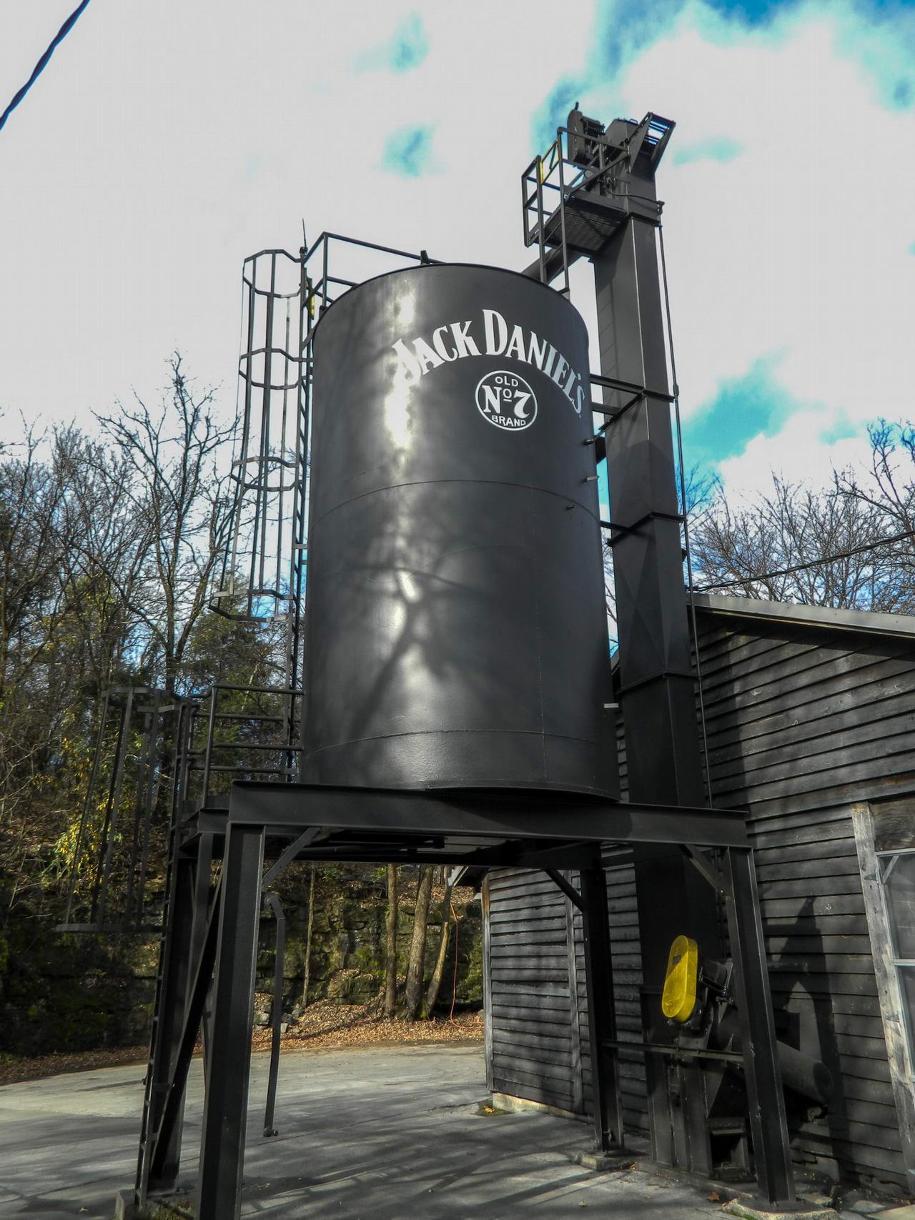 Černý zásobník s logem JACK DANIEL’S OLD No.7 BRAND u dřevěné budovy