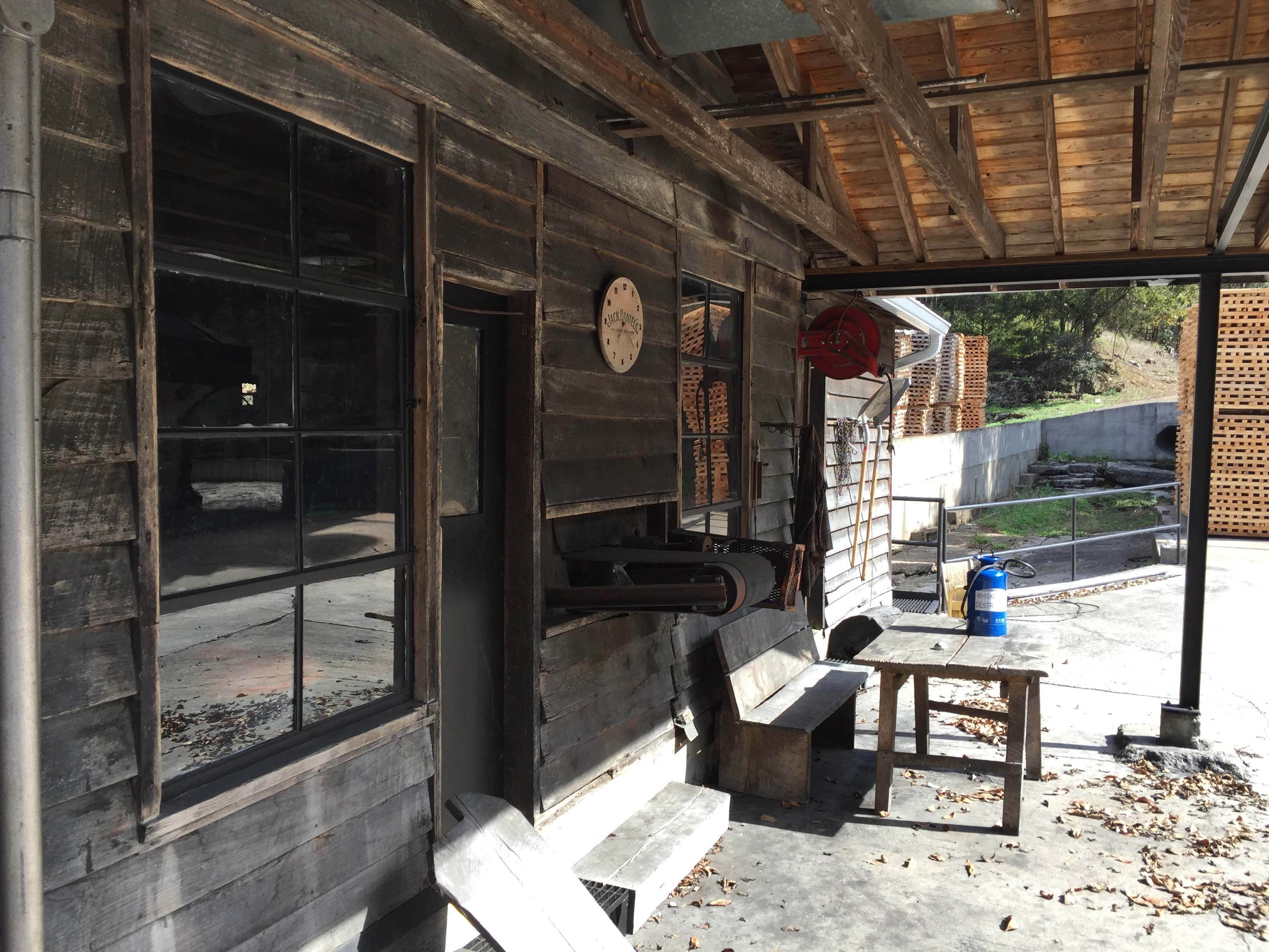 Dřevěná veranda staré budovy, cedule Jack Daniel’s, lavičky, hadice a palety