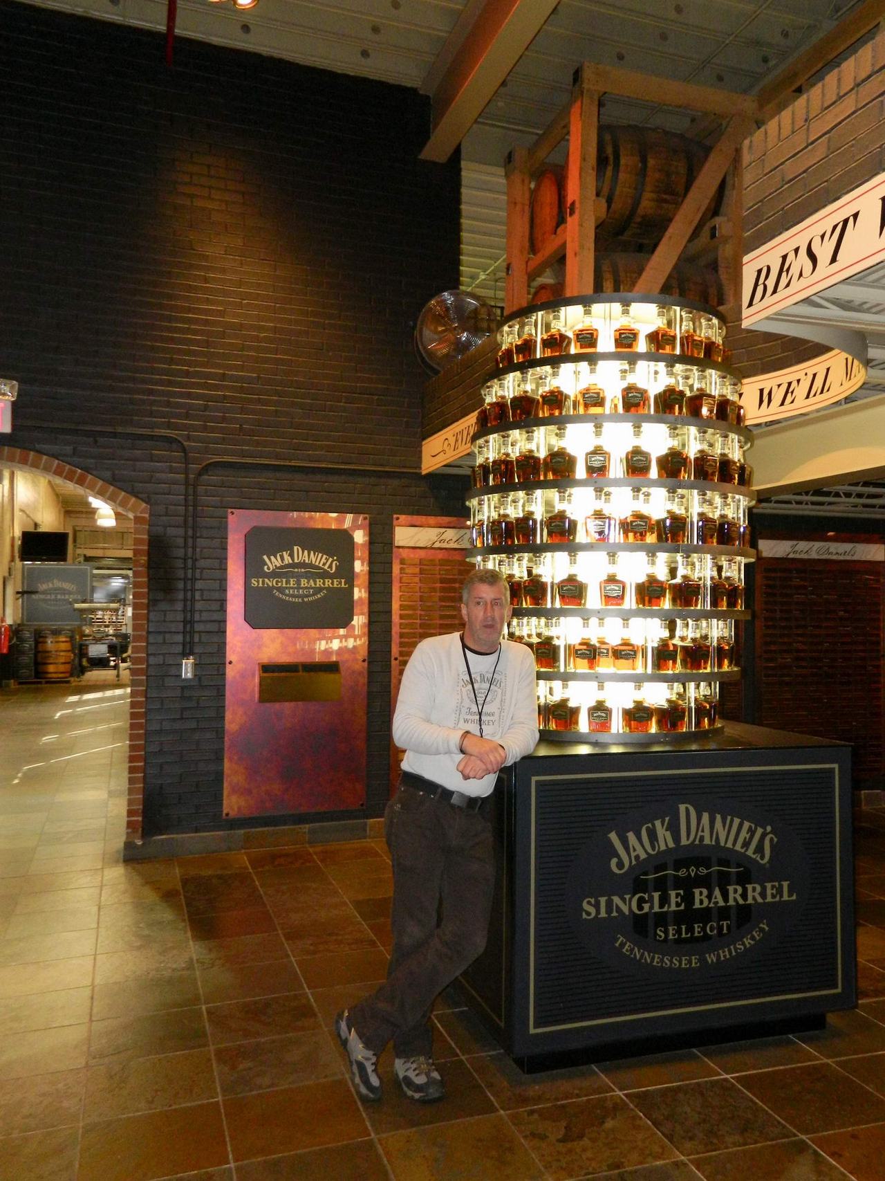 Muž opřený o osvětlený stojan s lahvemi Jack Daniel’s Single Barrel Select Tennessee Whiskey