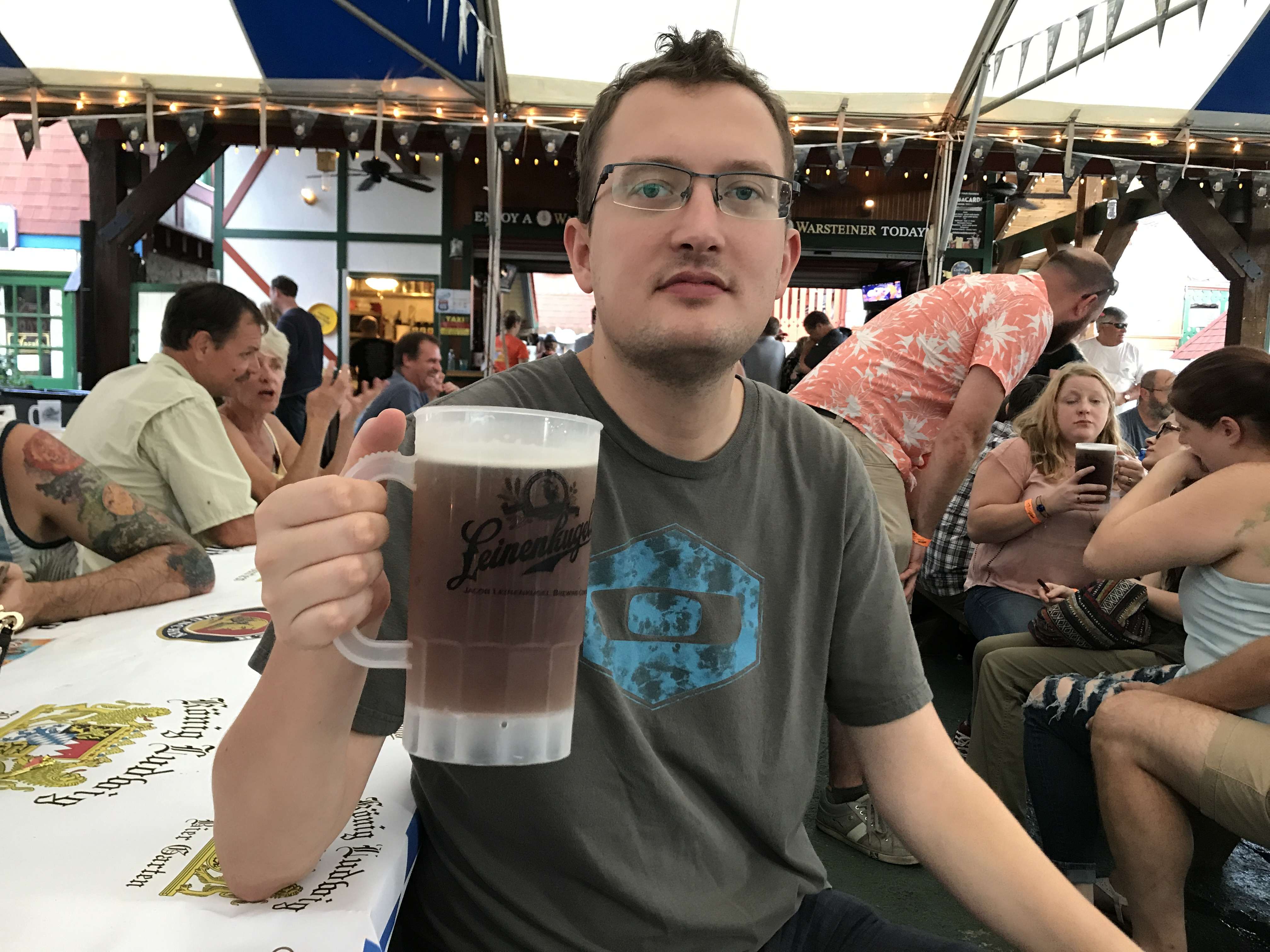 Muž s brýlemi drží korbel piva Leinenkugel's v pivním stanu.