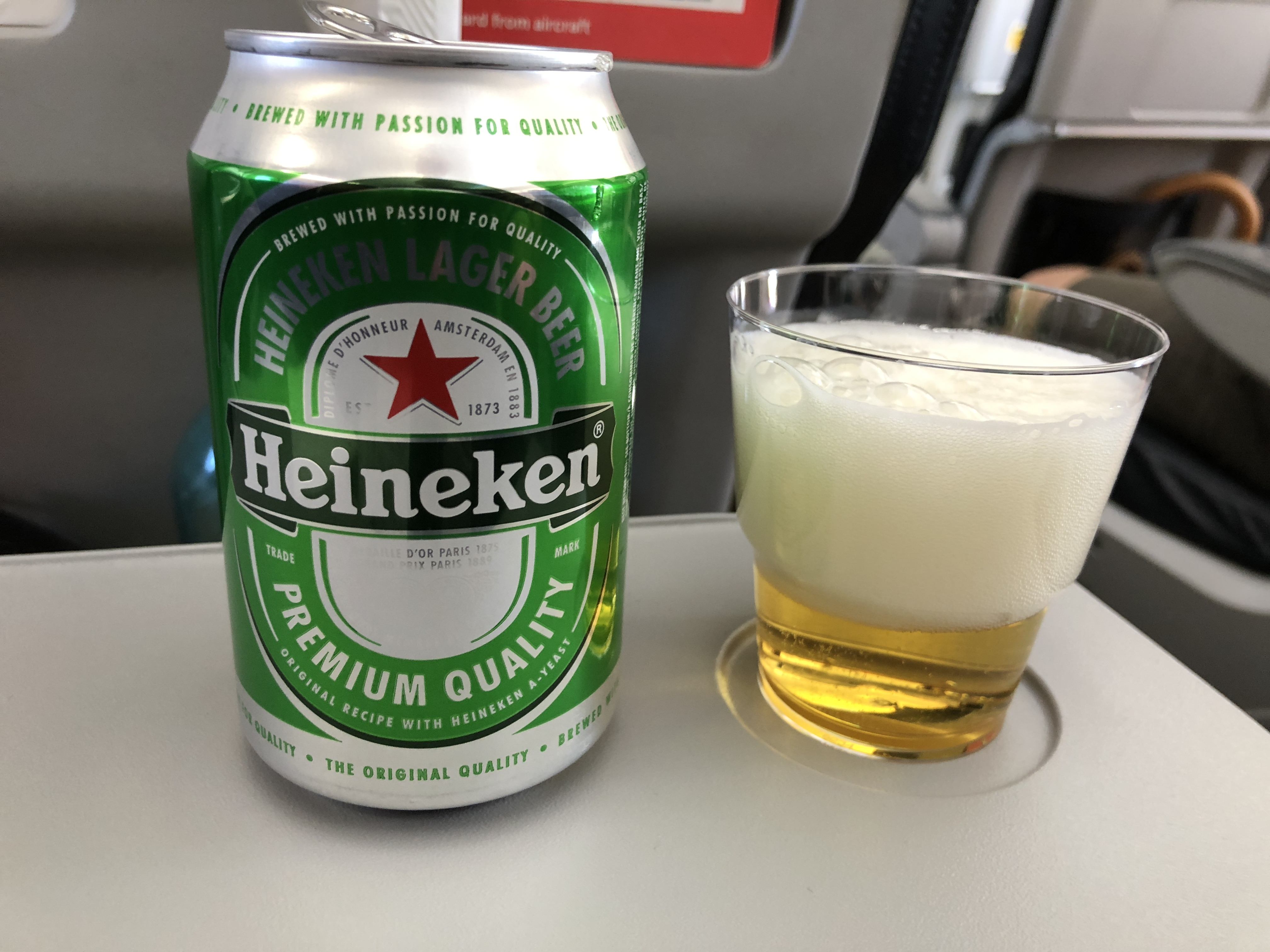Plechovka piva Heineken Lager Beer a plastový kelímek s pivem na stolku