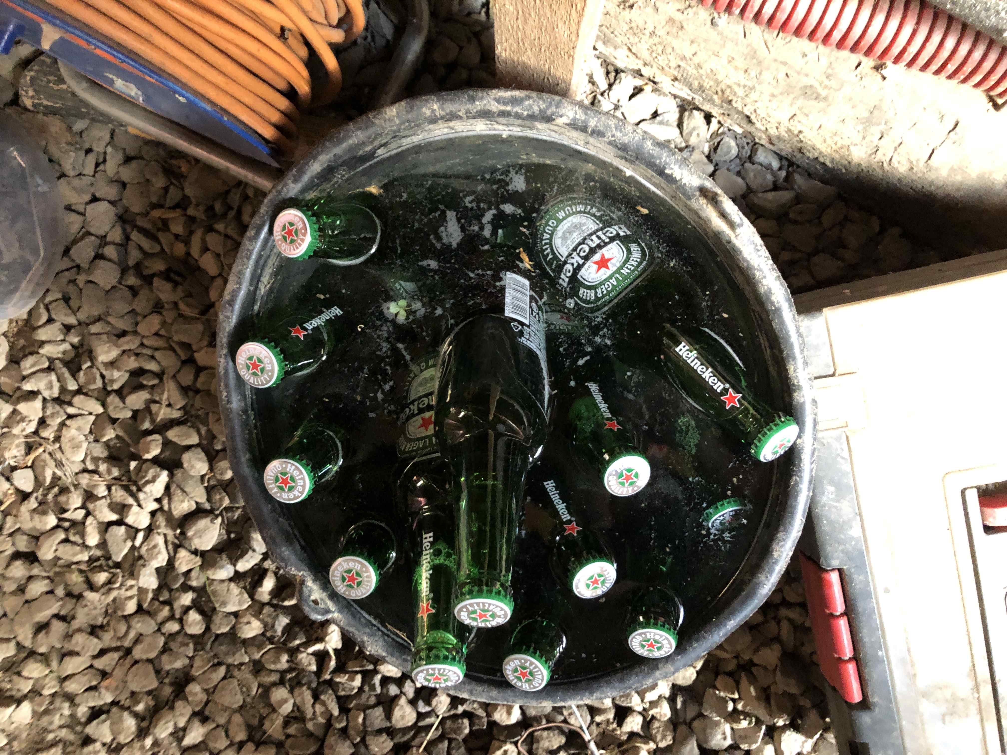 Plastový kyblík s vodou a prázdnými lahvemi piva Heineken na štěrku