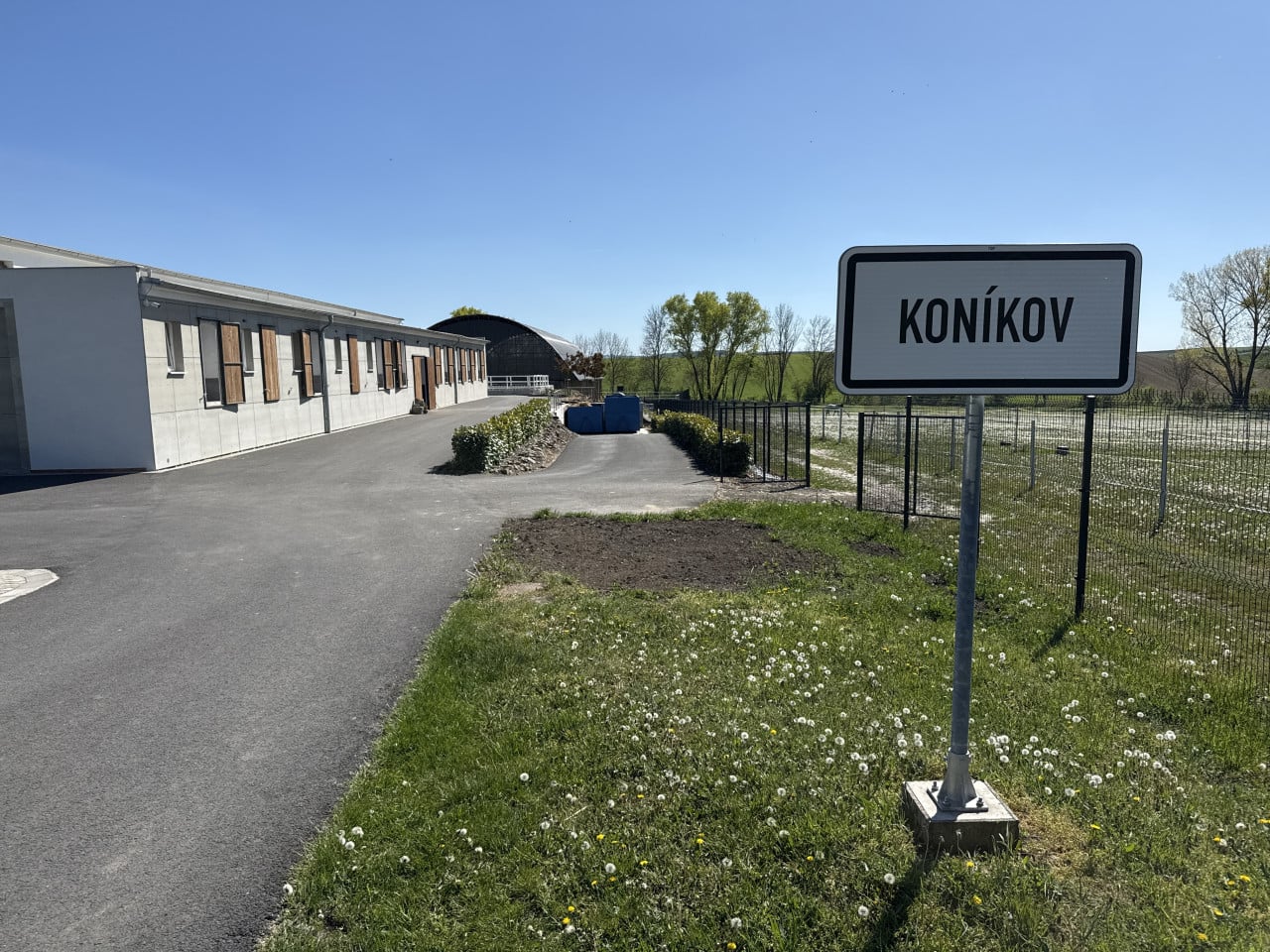 Jezdecká stáj s budovou a cedulí KONÍKOV u silnice na louce
