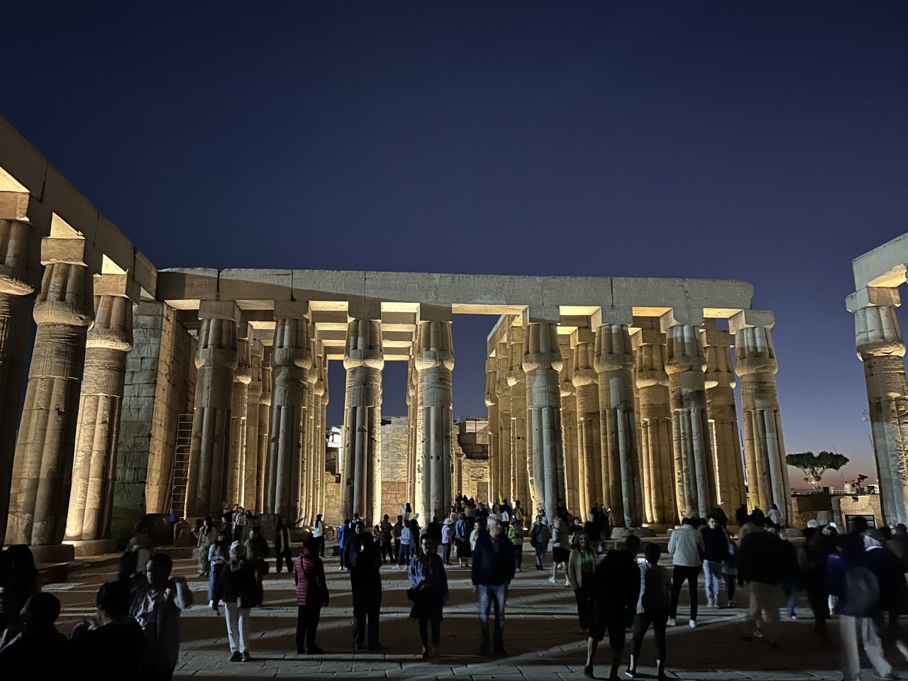 Noční osvětlený chrám Karnak s monumentálními sloupy a návštěvníky na nádvoří
