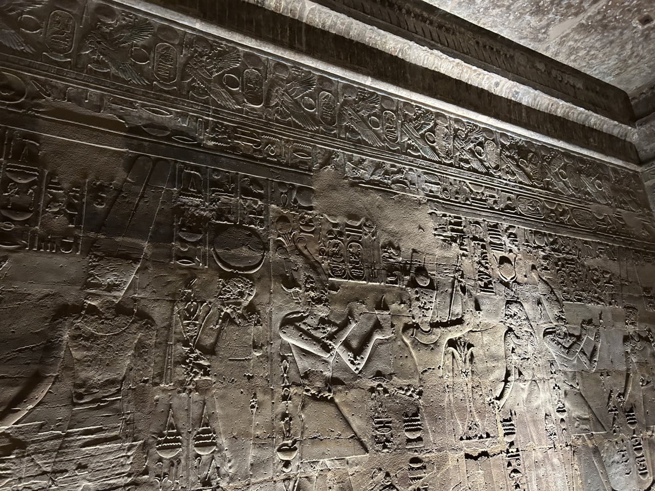 Reliéfní hieroglyfy s postavami a okřídlenými motivy na kamenné stěně Karnaku