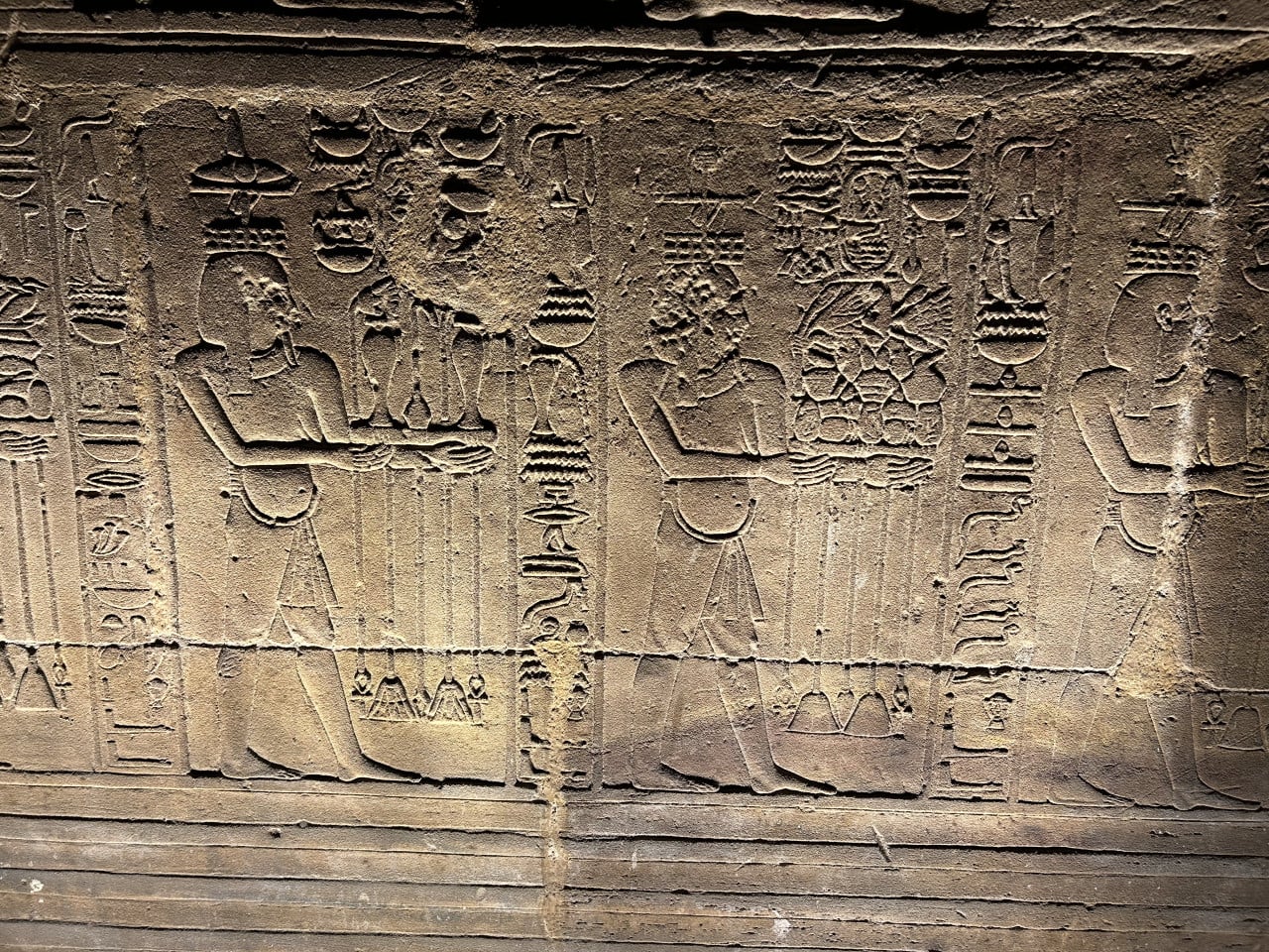 Reliéf s egyptskými božstvy a hieroglyfy vytesaný do kamenné stěny
