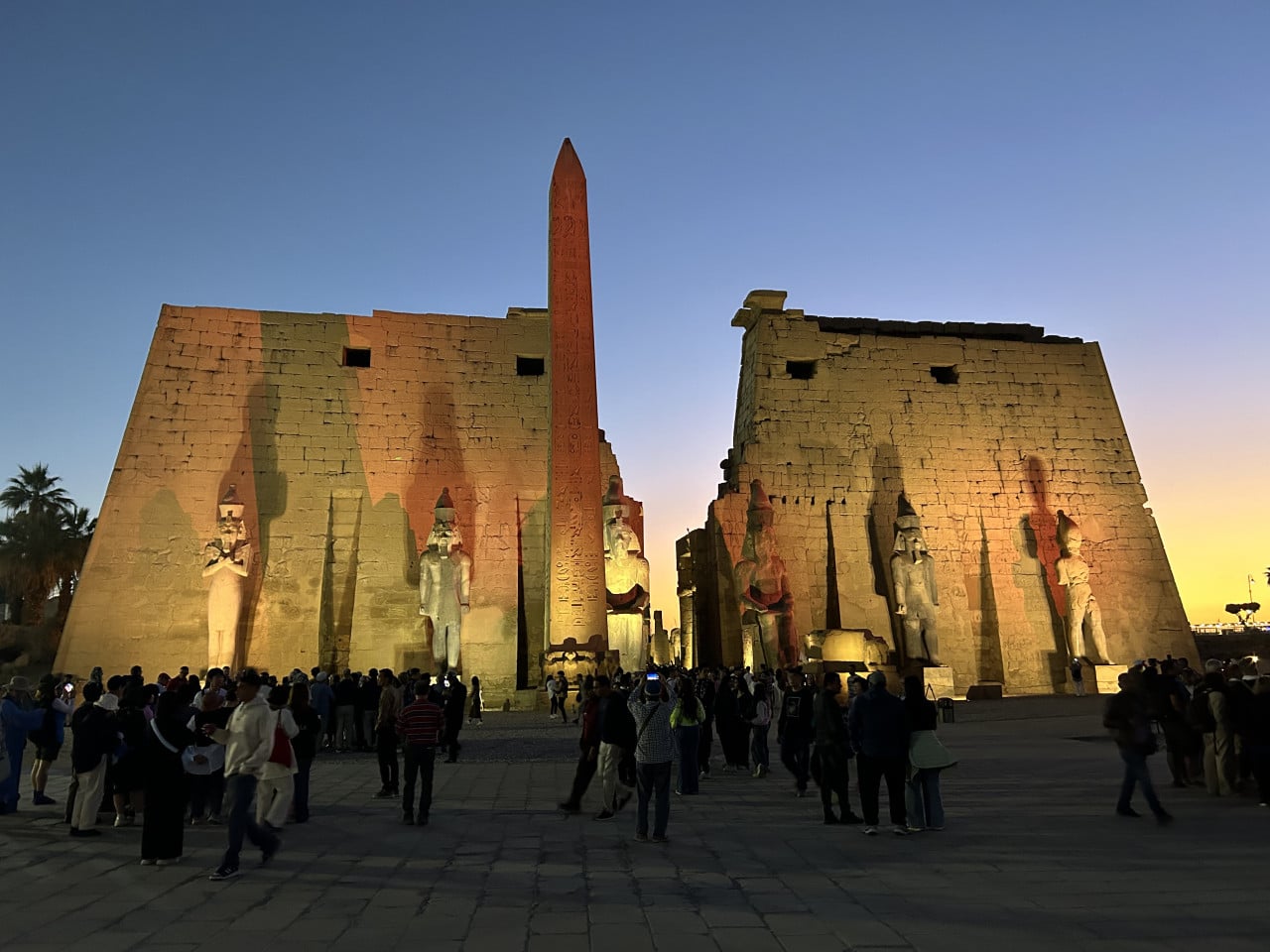 Osvětlený vstup do chrámu Karnak s obeliskem a sochami za soumraku