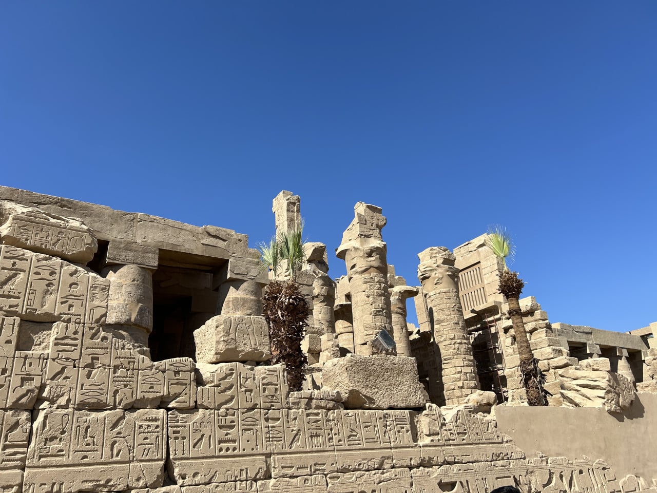 Ruiny chrámu Karnak s hieroglyfy, sloupy a modrou oblohou.