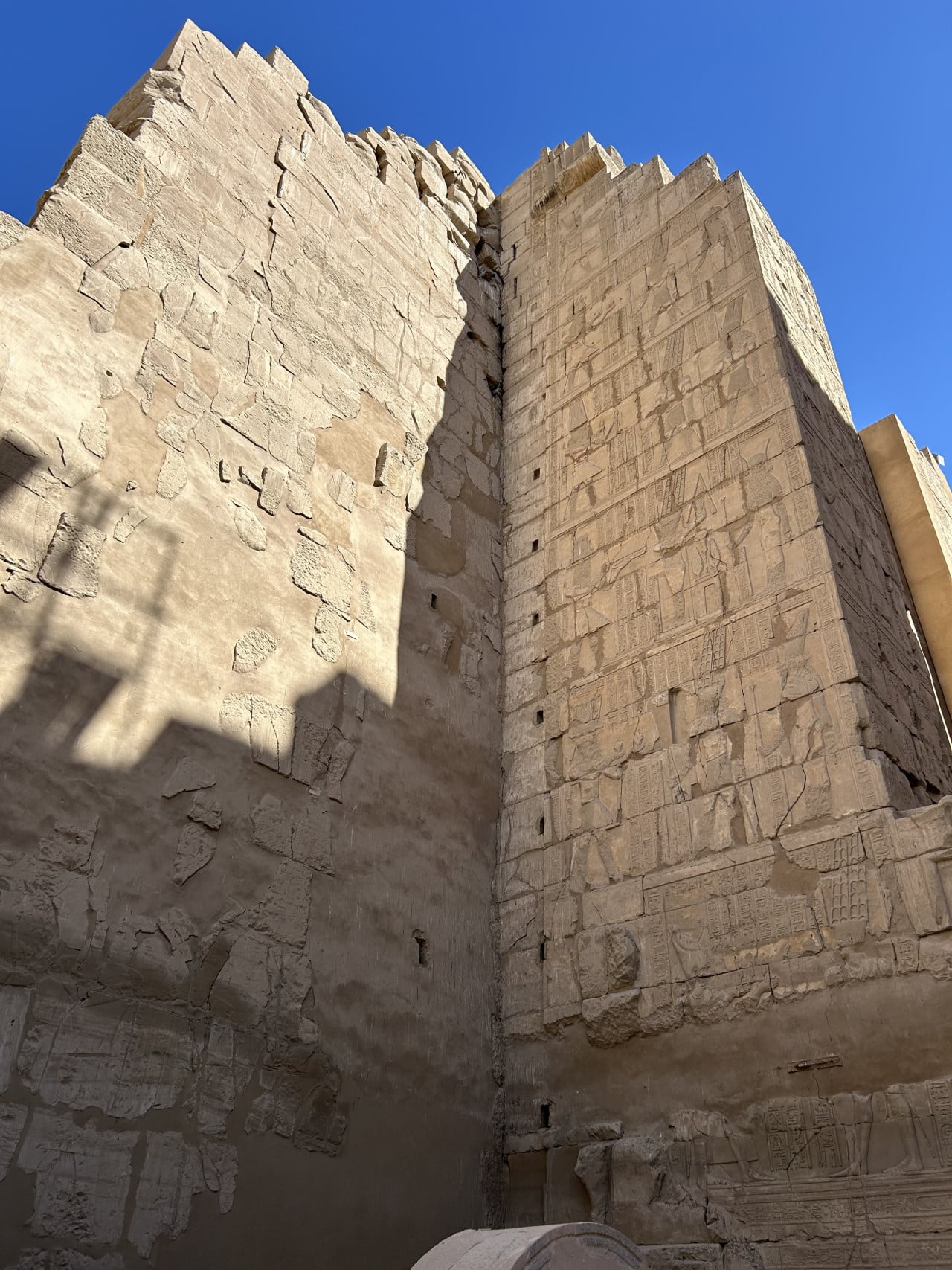 Monumentální kamenné zdi chrámu Karnak s hieroglyfy pod modrou oblohou
