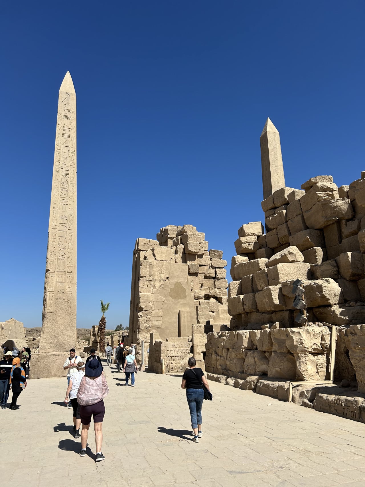 Návštěvníci u vysokých egyptských obelisků a ruin v chrámu Karnak