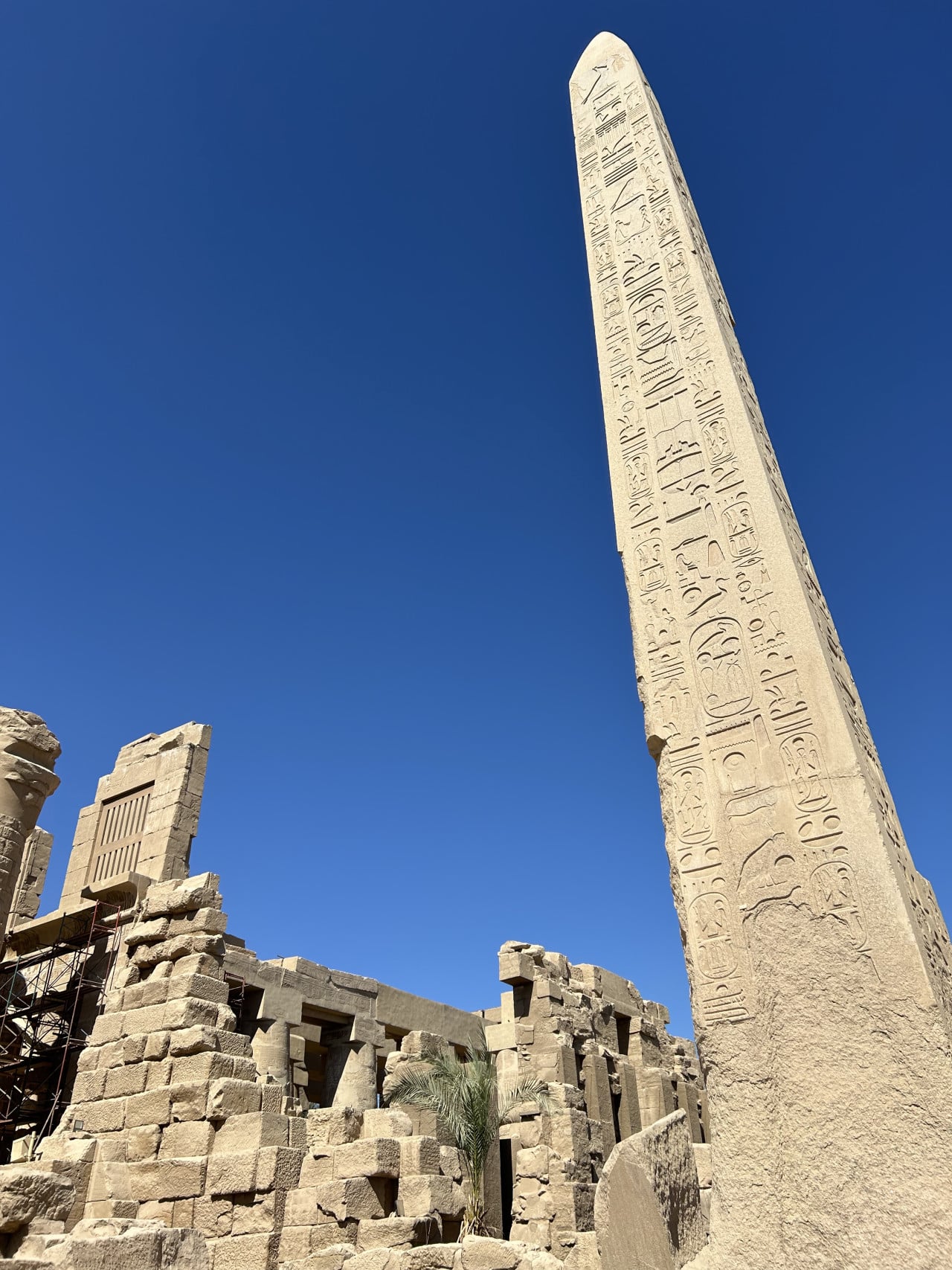 Egyptský obelisk s hieroglyfy nad ruinami chrámu proti modré obloze