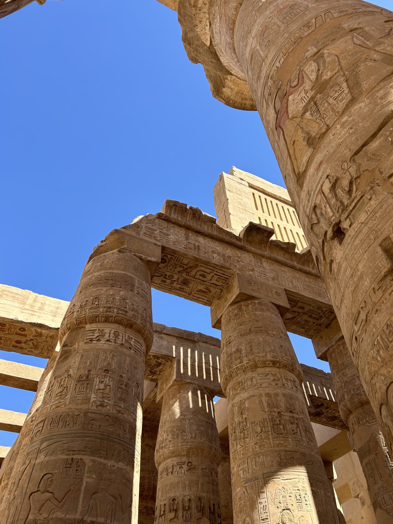 Nízký pohled na obří hieroglyfické sloupy chrámu Karnak pod modrou oblohou