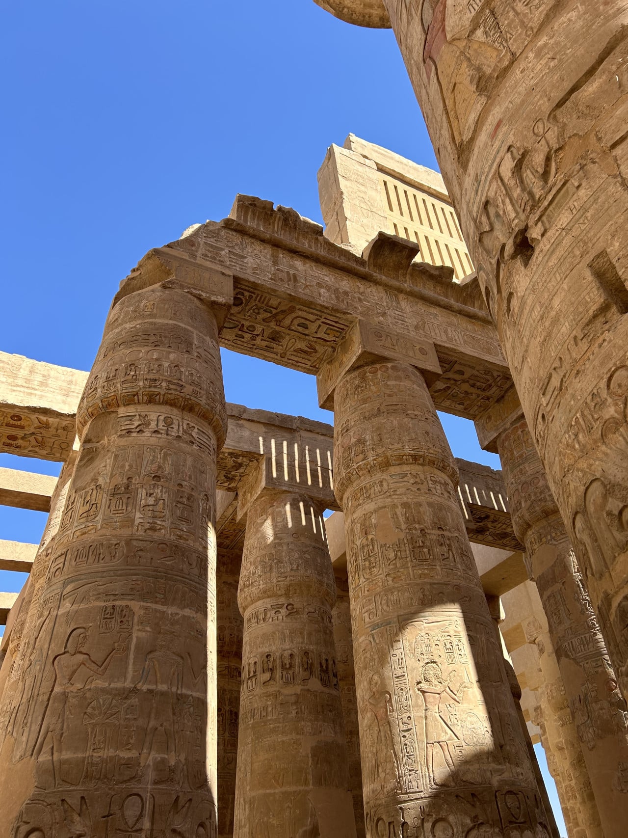 Kamenné sloupy chrámu Karnak s hieroglyfy proti modré obloze