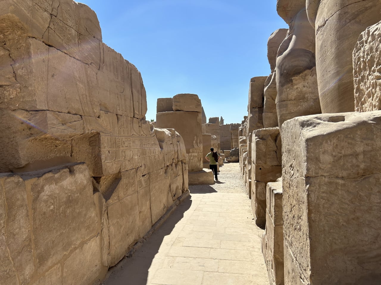 Úzká cesta mezi monumentálními kamennými bloky chrámu Karnak s jednou postavou vpředu
