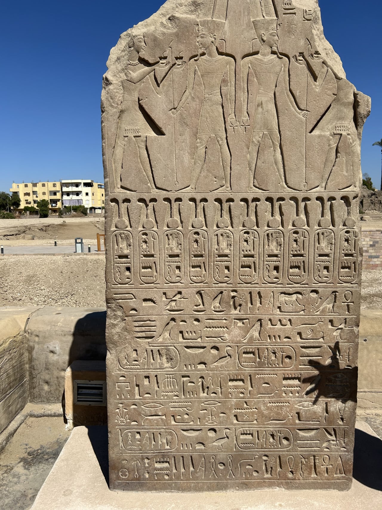 Vytesaný egyptský obelisk s hieroglyfy a postavami bohů na slunci