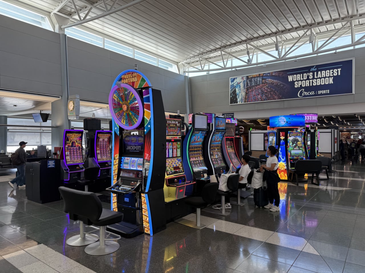 Automaty a Wheel of Fortune v letištní hale; banner the WORLD'S LARGEST SPORTSBOOK