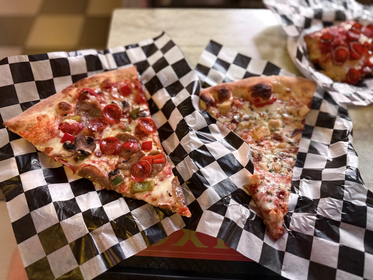 Dva velké kusy pizzy na černobílém kostkovaném papíru na stole