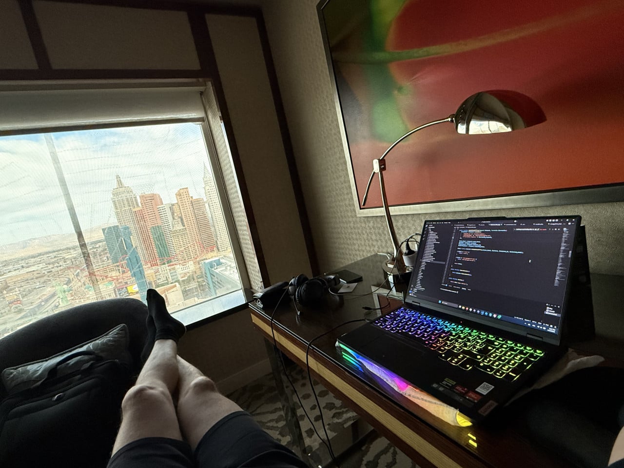 Výhled z hotelového pokoje na Las Vegas, notebook s kódem na stole, nohy na gauči