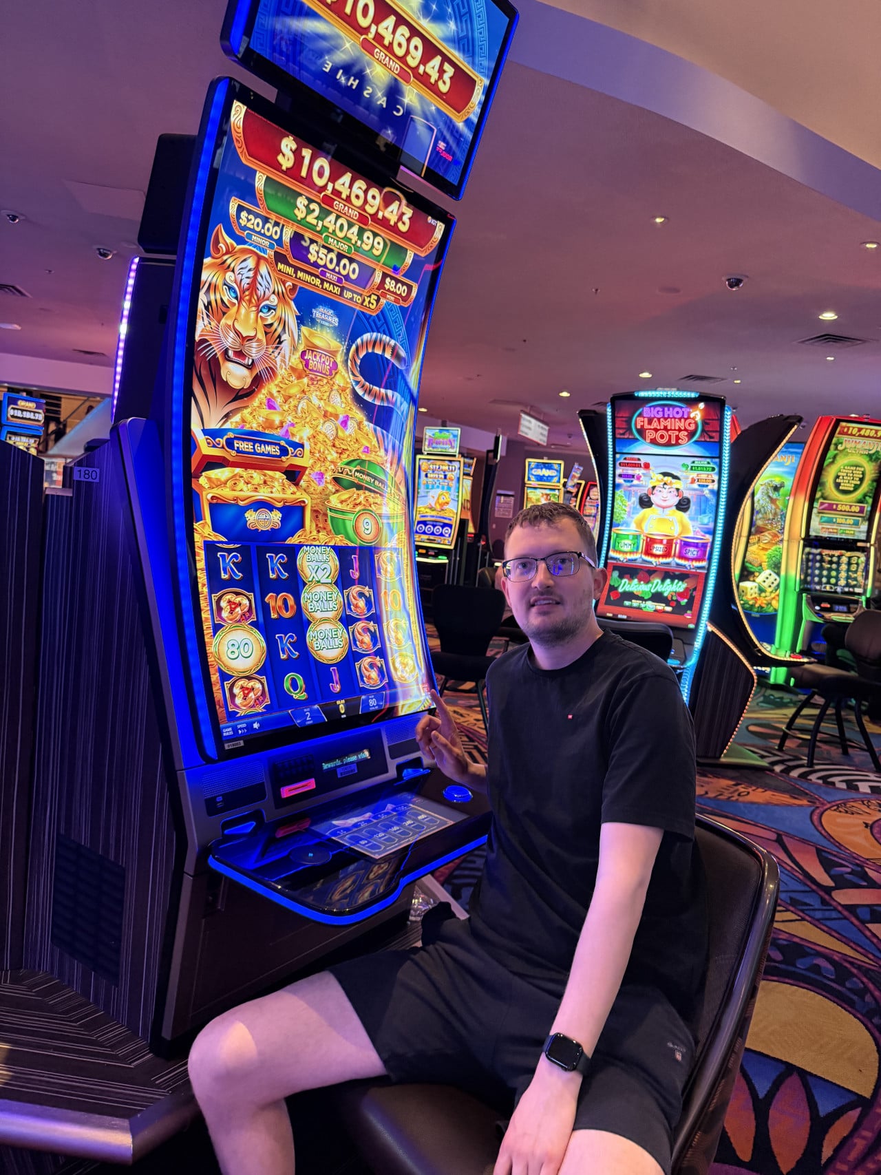 Muž v kasinu u hracího automatu s tygrem, nápis $10,469.43, FREE GAMES.