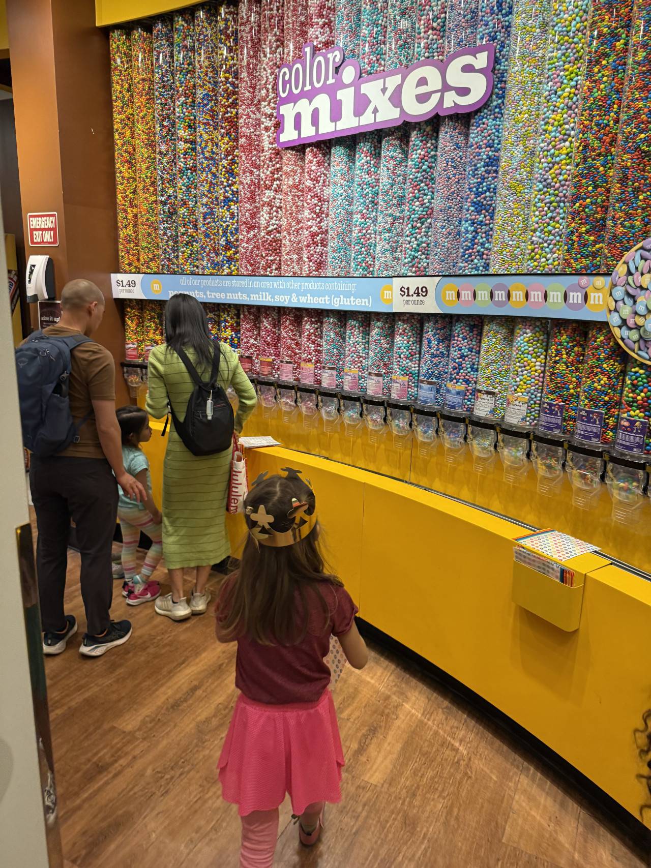 Rodina před stěnou M&M’s, nápis color mixes, cena $1.49 per ounce.