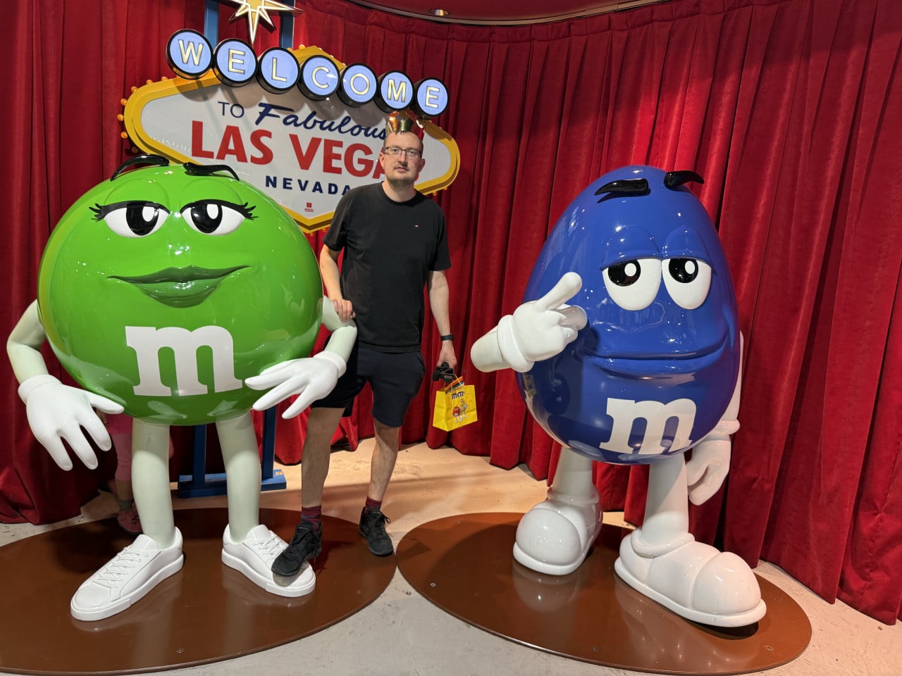 Muž mezi sochami zeleného a modrého M&M, před nápisem WELCOME to Fabulous LAS VEGAS NEVADA.
