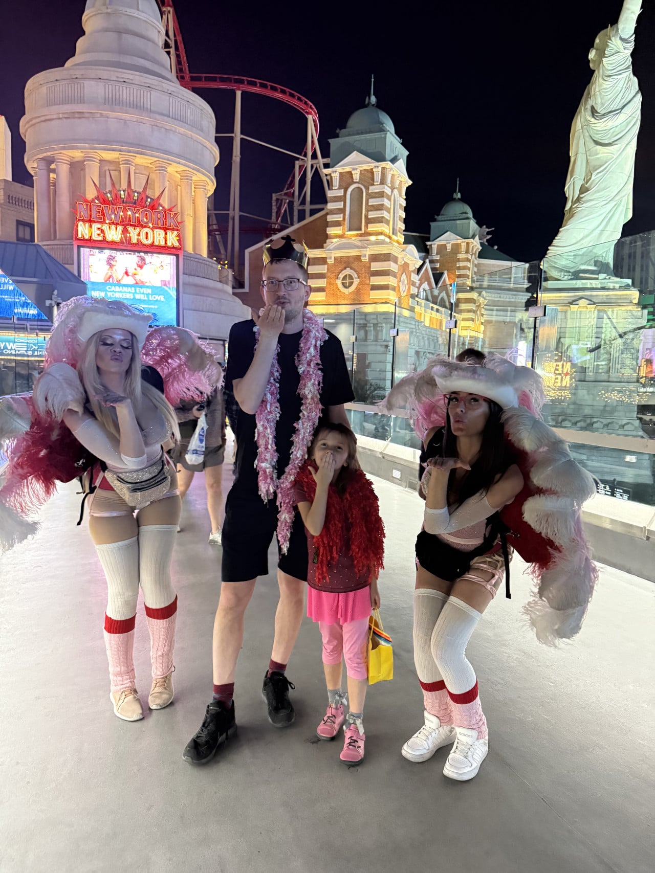 Muž s dívkou a dvě showgirls pózují pod nápisem NEW YORK NEW YORK.