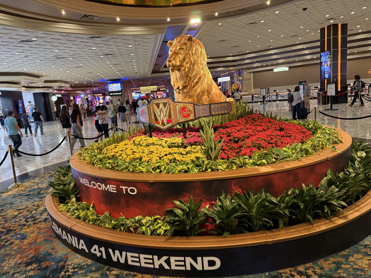 Zlatý lev s páskem WWE u květin; nápis WELCOME TO MANIA 41 WEEKEND.