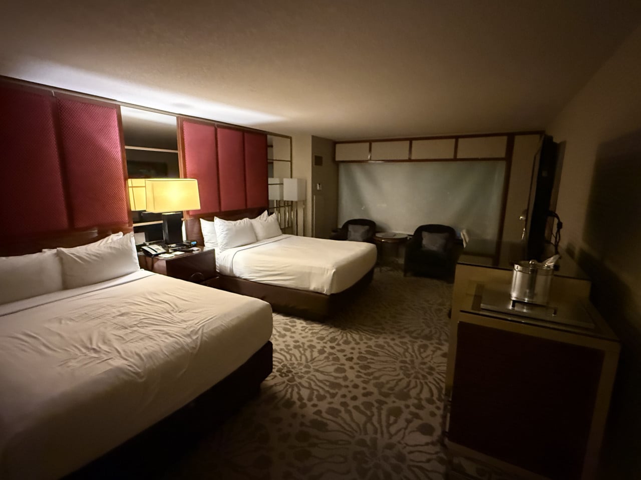 Hotelový pokoj v Las Vegas se dvěma postelemi, lampou, křesly a televizí.