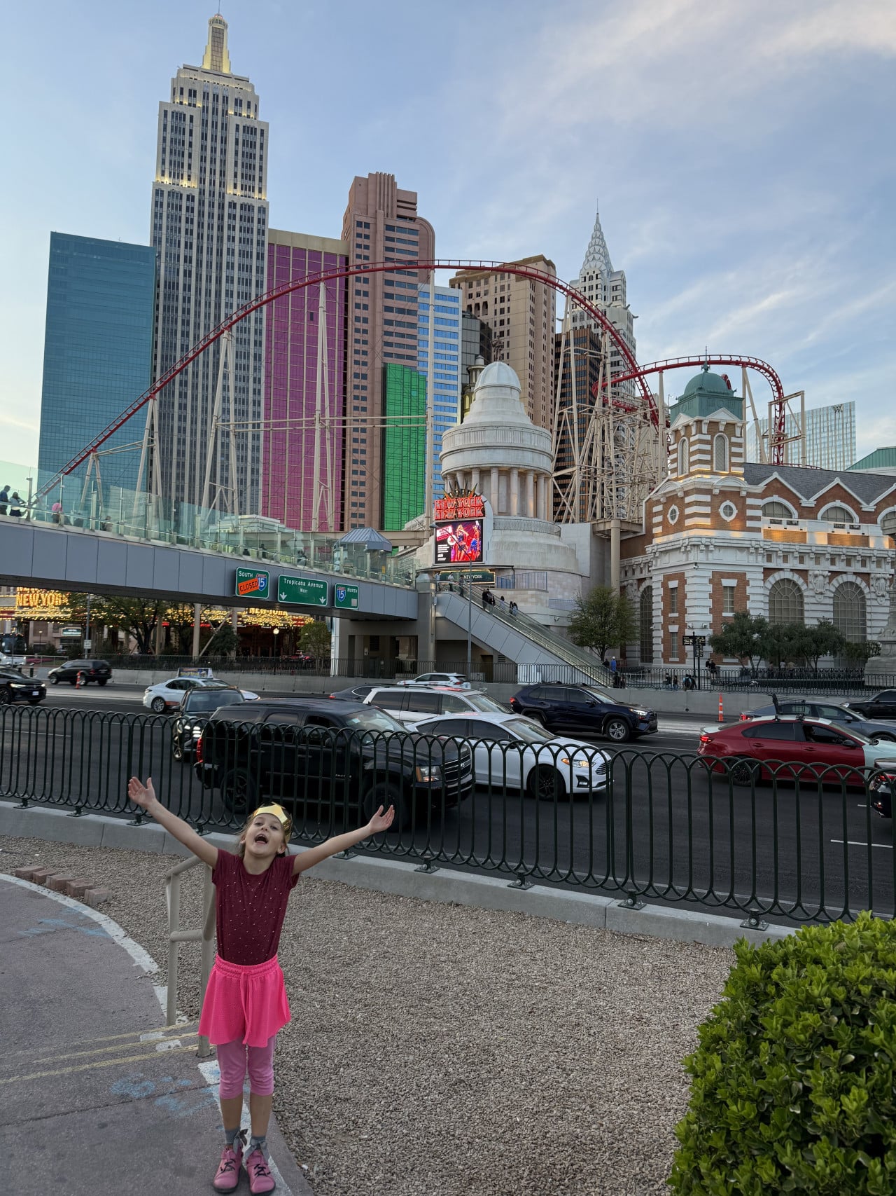 Dívka s rozpaženýma rukama před hotelem New York-New York a horskou dráhou