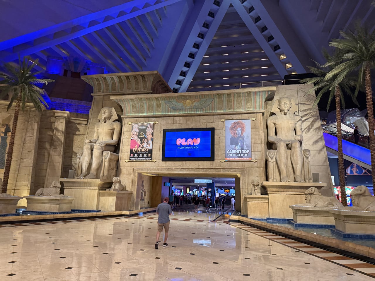 Vstup do Luxoru s egyptskými sochami, nápis PLAYGROUND, plakáty FANTASY a CARROT TOP.