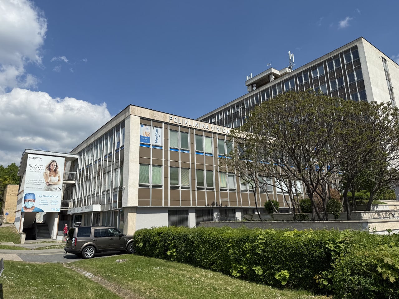 Budova Poliklinika Viniční s nápisy NeoVize a Medicon Clinic pod modrou oblohou.