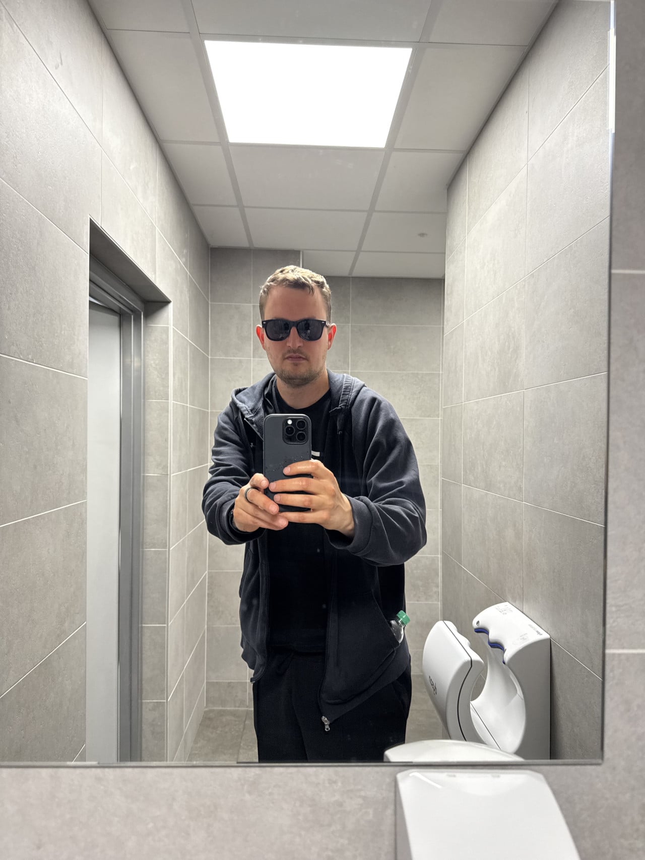 Muž v brýlích a mikině se fotí v zrcadle na toaletě kliniky NeoVize Brno.