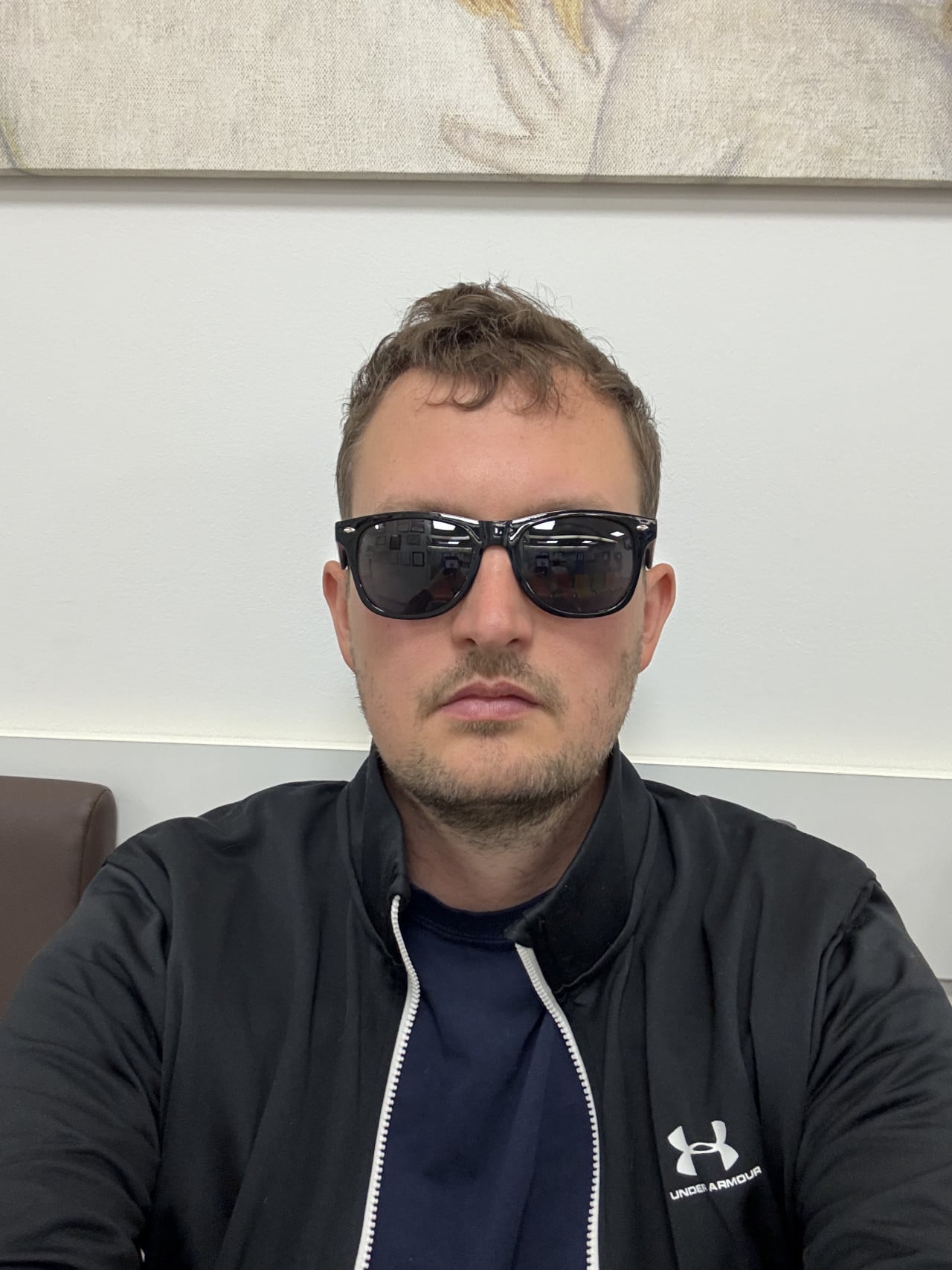 Muž v tmavé bundě a slunečních brýlích sedí v ordinaci po laserové operaci očí.