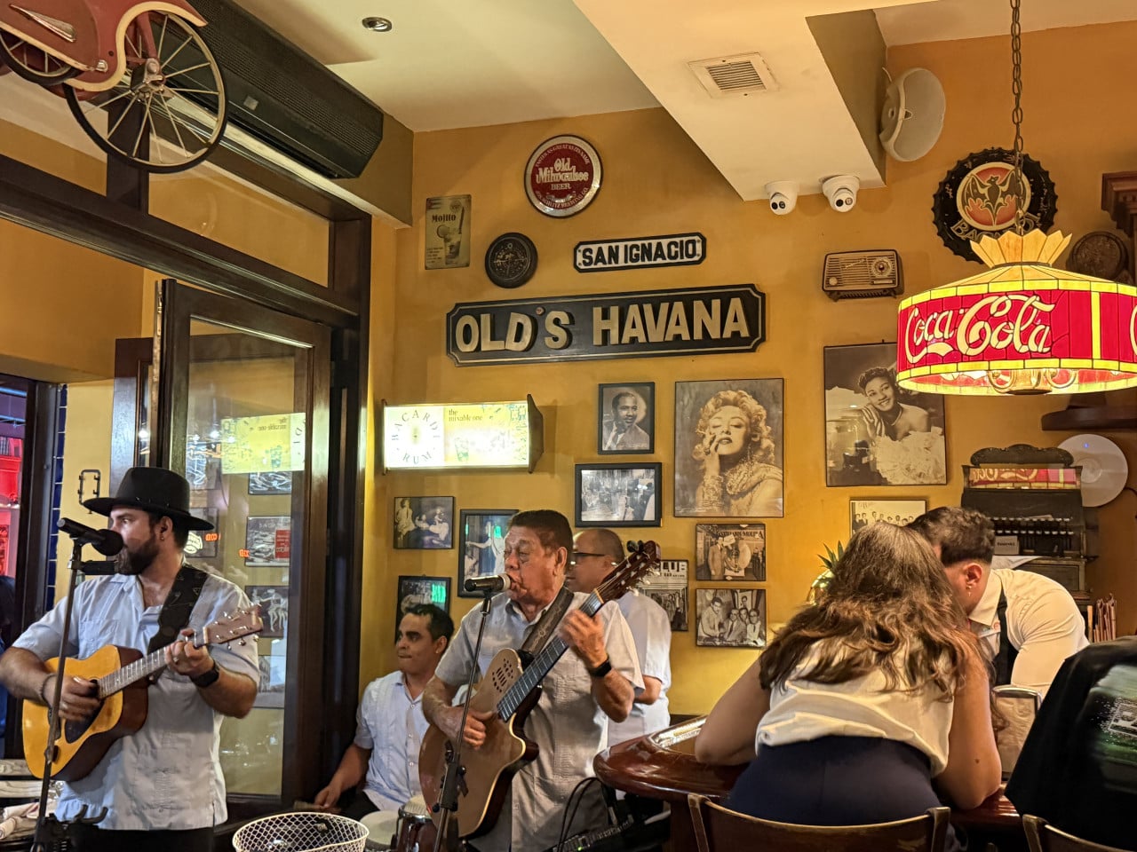 Kapela hraje v podniku OLD'S HAVANA, nápisy SAN IGNACIO a Coca-Cola.