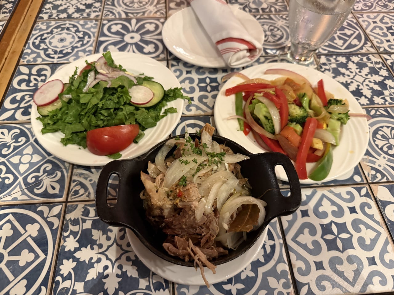 Trhané vepřové s cibulí v misce, salát a zelenina na talířích