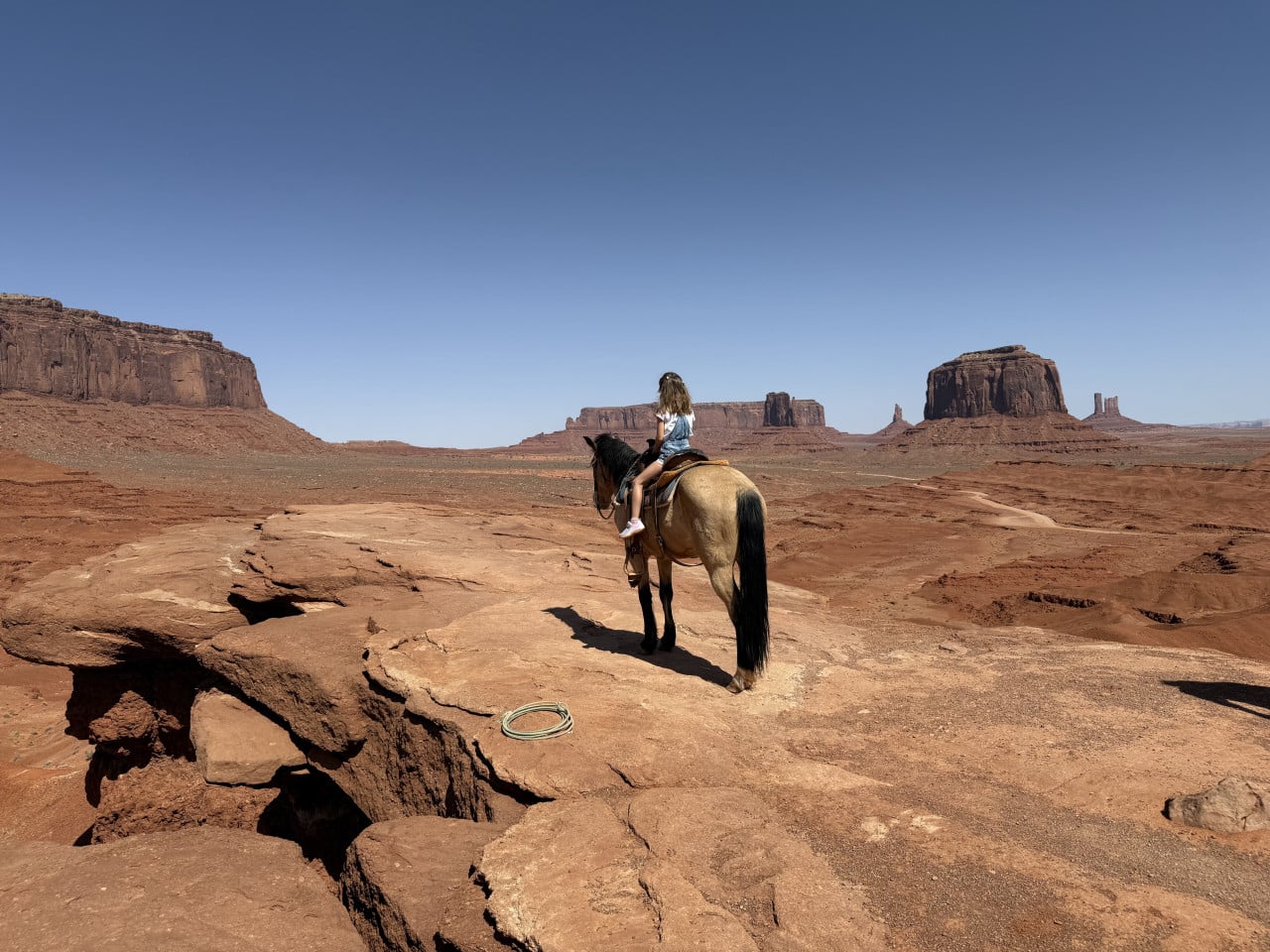 Jezdkyně na koni na skalní plošině, v pozadí monumenty Monument Valley.