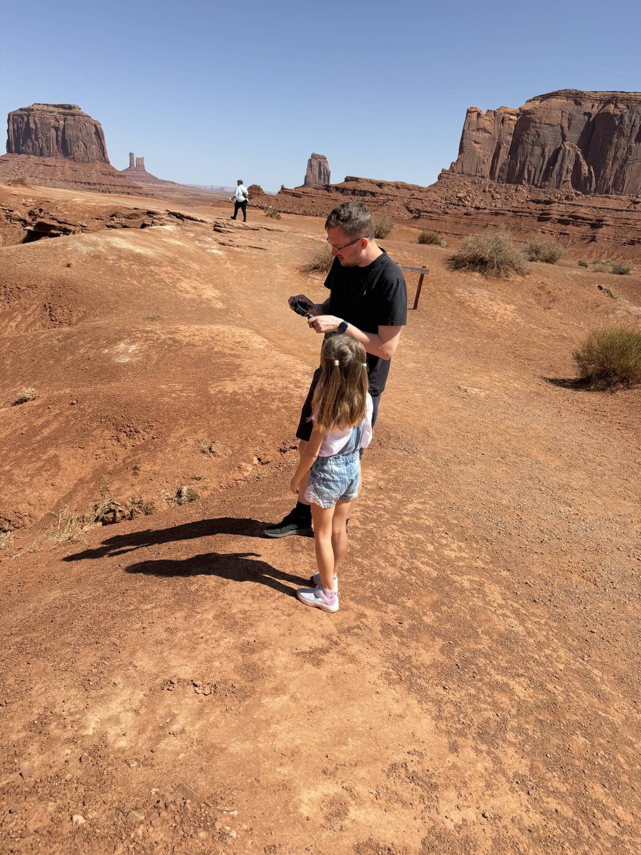 Muž s fotoaparátem a holčička na skále, v pozadí monumenty Monument Valley
