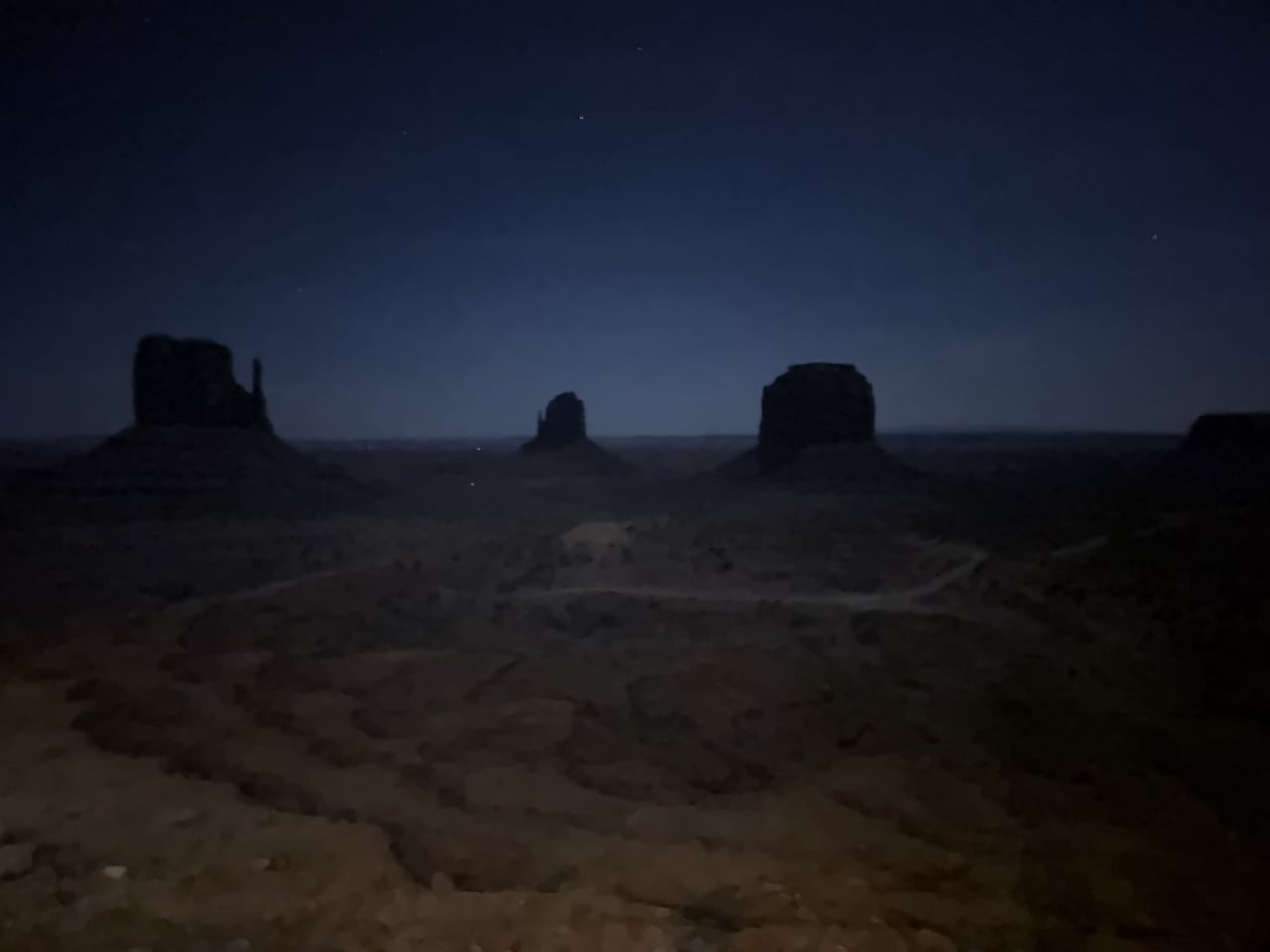 Noční panorama Monument Valley, siluety skalních monumentů pod hvězdnou oblohou