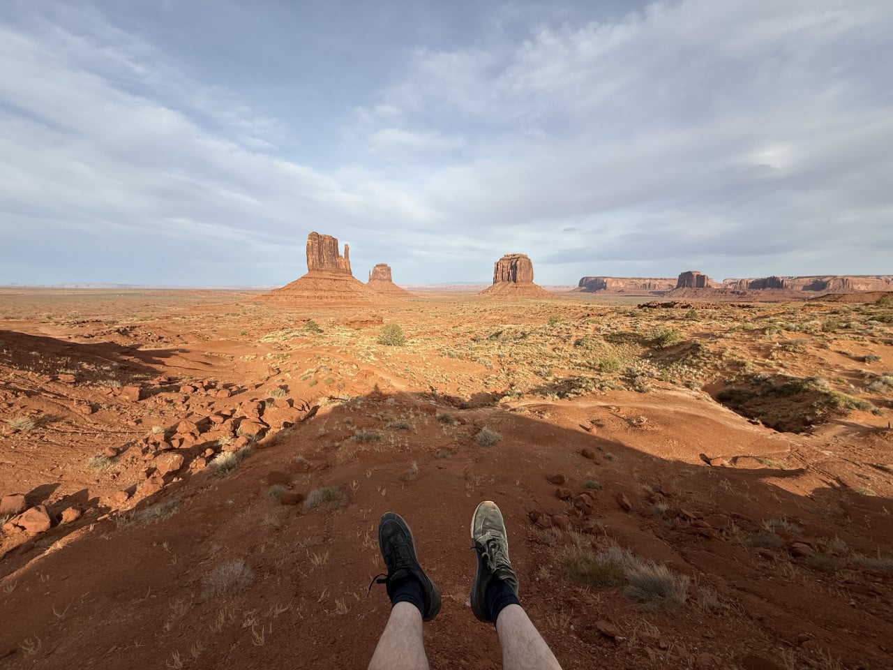 Nohy v botách na červené skále, v dálce monumenty Monument Valley