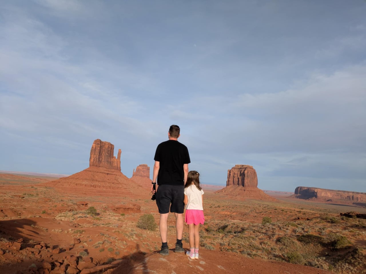 Muž a malá dívka stojí zády, hledí na skalní věže Monument Valley.