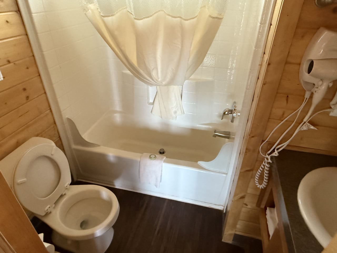 Malá koupelna v dřevěné chatce: vana se závěsem, toaleta a umyvadlo.