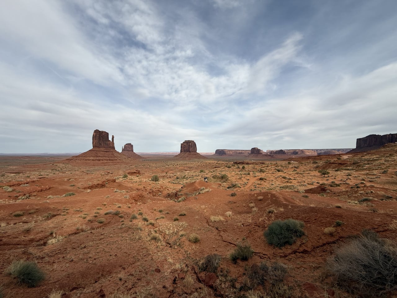 Široký pohled na červenou poušť Monument Valley s ikonickými skalními věžemi pod zataženou oblohou