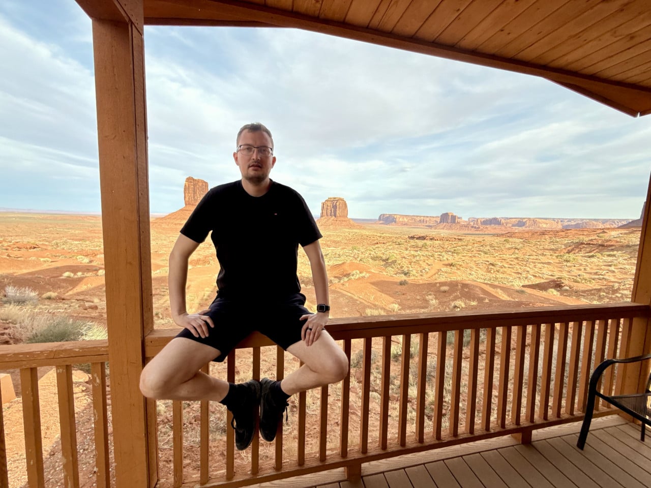 Muž sedí na dřevěné verandě, za ním skalní monumenty Monument Valley