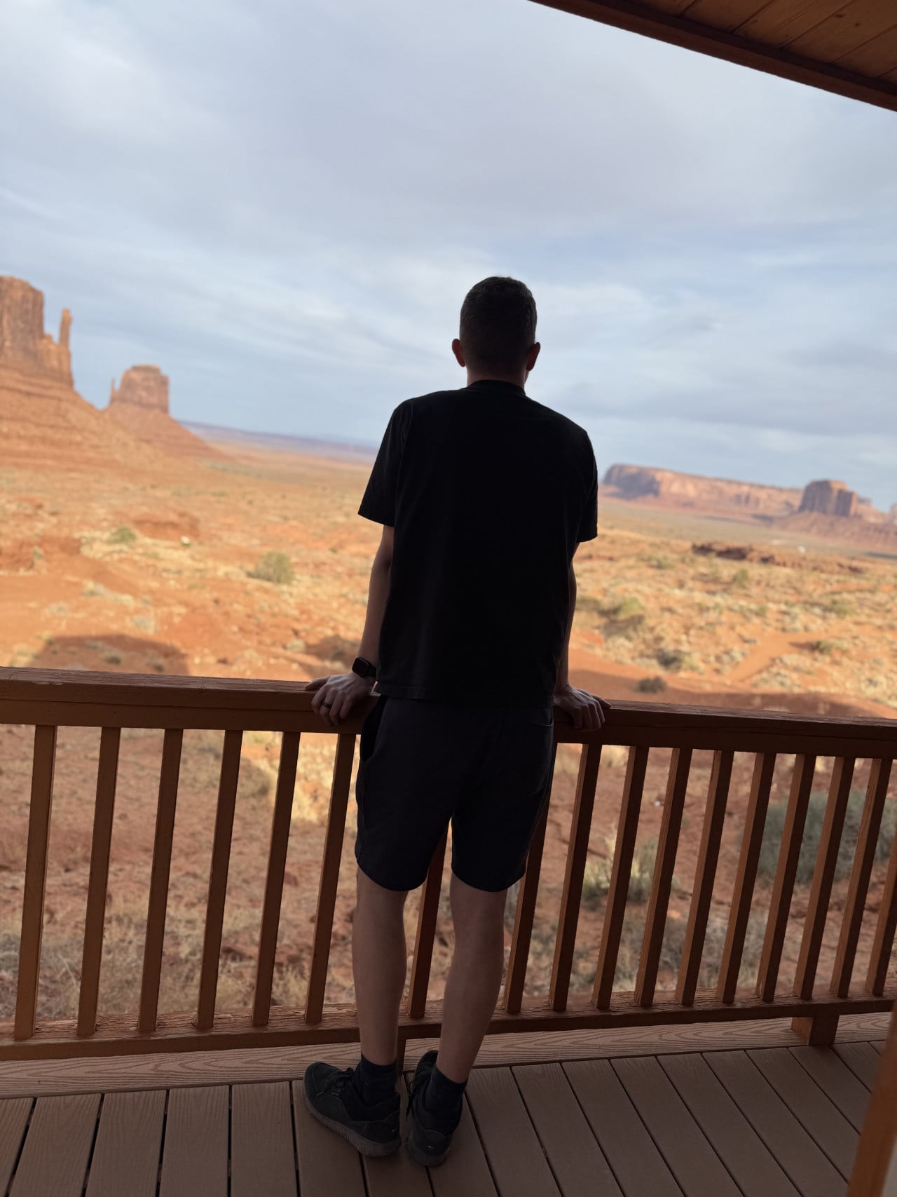 Postava na verandě chatky hledí na skalní monumenty Monument Valley