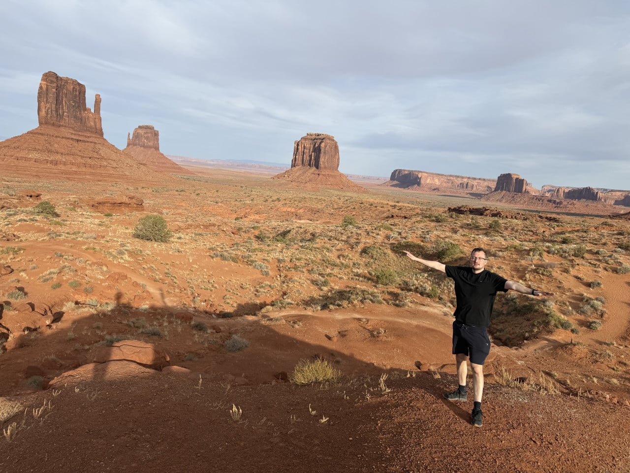 Muž s rozpaženýma rukama na vyhlídce, za ním monumenty Monument Valley