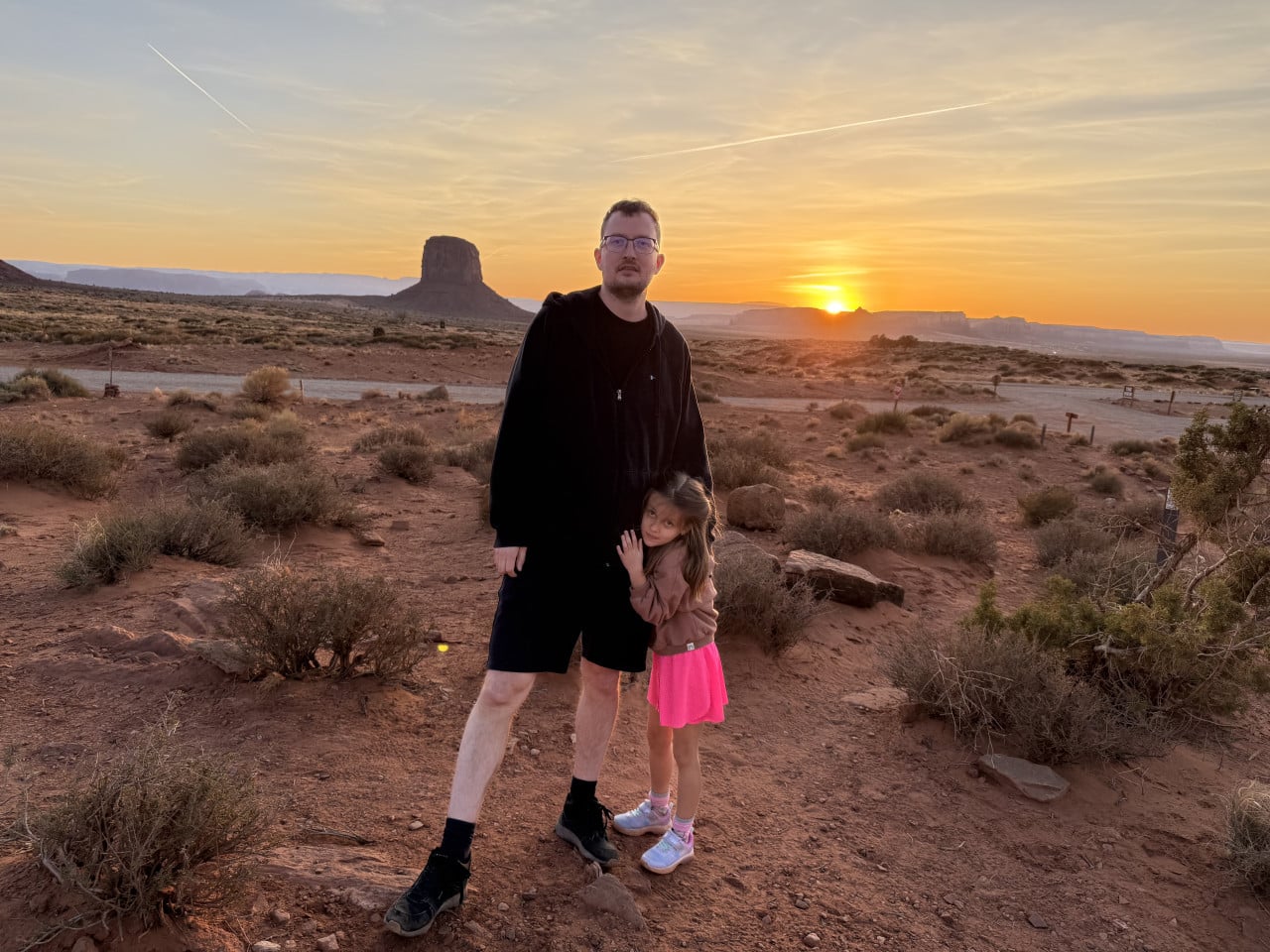 Muž s dívkou v poušti Monument Valley při západu slunce, v pozadí skalní věž